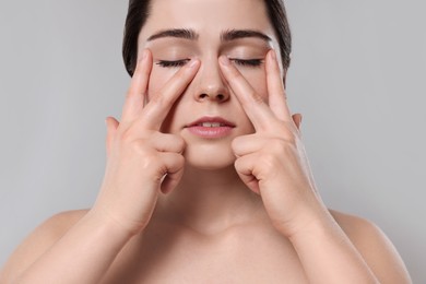 Photo of Young woman massaging her face on grey background