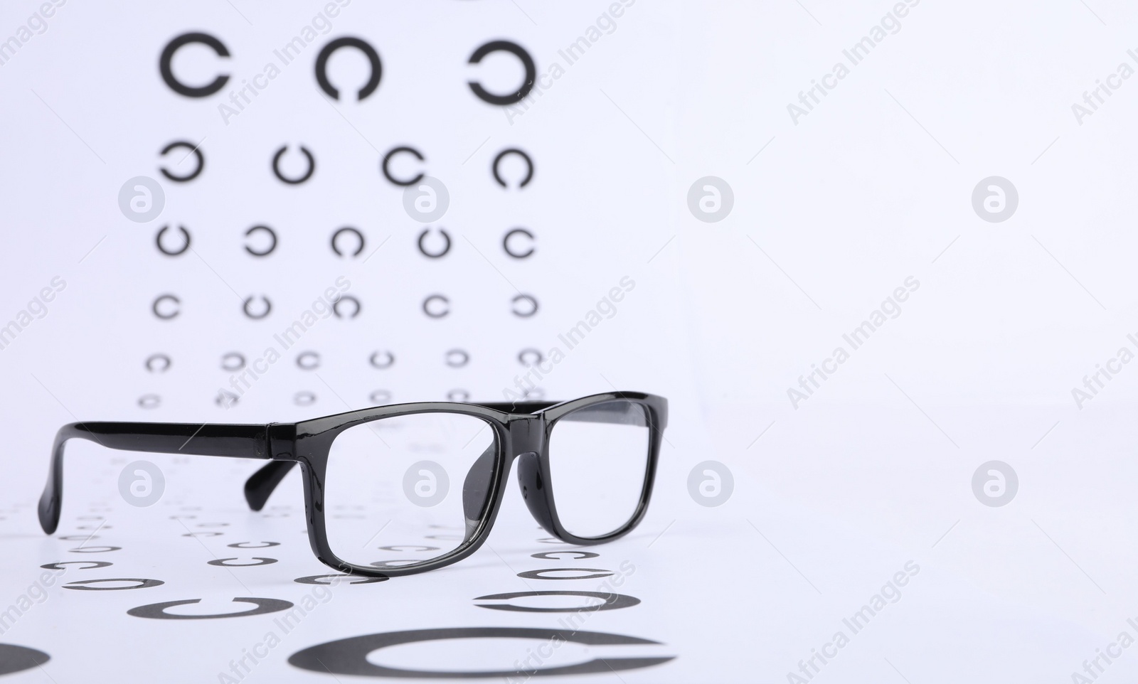 Photo of Vision test chart and glasses on white background, closeup. Space for text