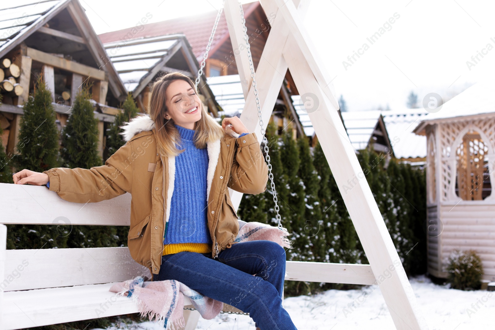 Photo of Young woman in warm clothes resting on outdoor swing. Winter vacation