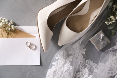 Flat lay composition with wedding rings, white high heel shoes and veil on grey background