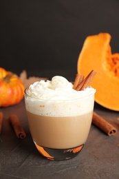 Glass with pumpkin spice latte and whipped cream on table