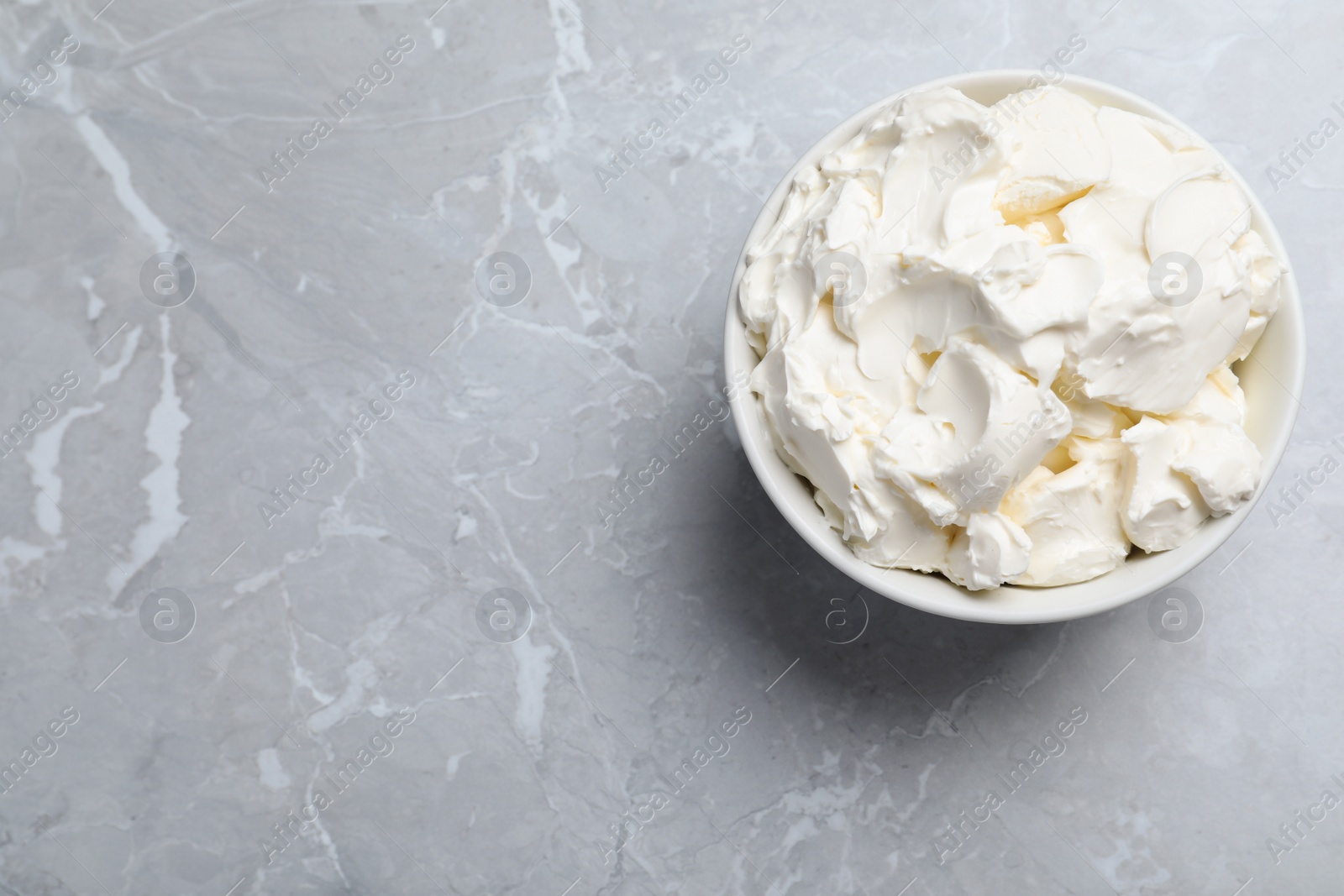 Photo of Bowl of tasty cream cheese on light grey marble table, top view. Space for text