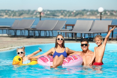 Photo of Happy family with inflatable rings in outdoor swimming pool on sunny summer day