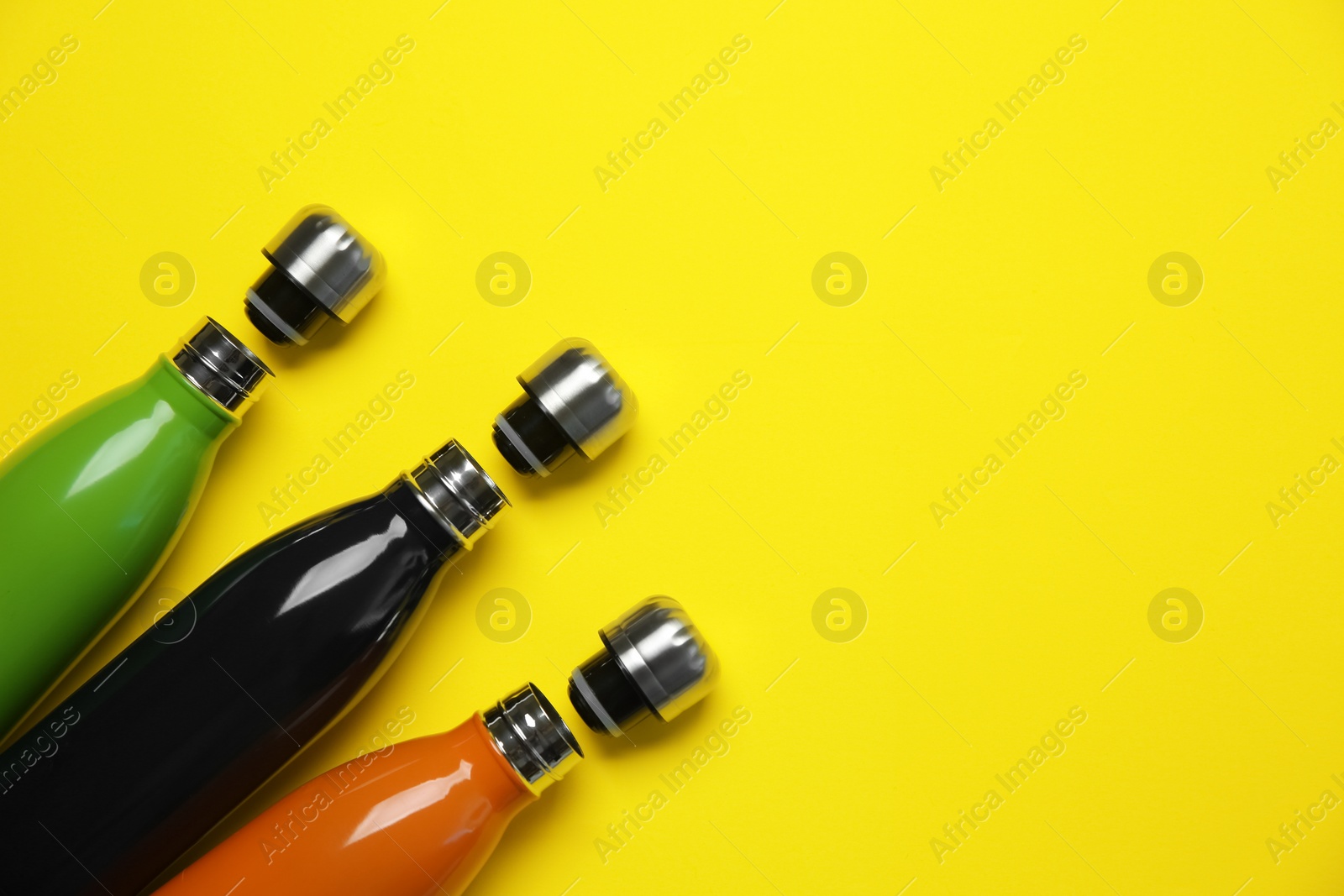 Photo of Different thermo bottles on yellow background, flat lay. Space for text