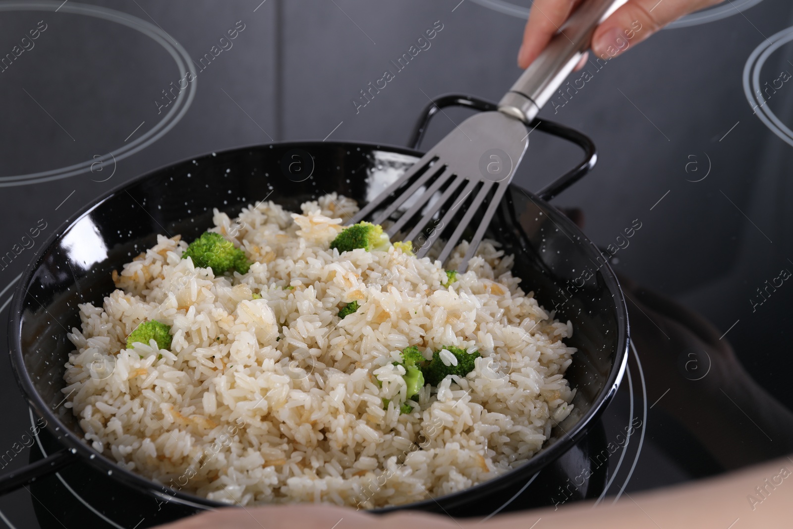 Photo of Woman frying rice with vegetables at induction stove in kitchen, closeup