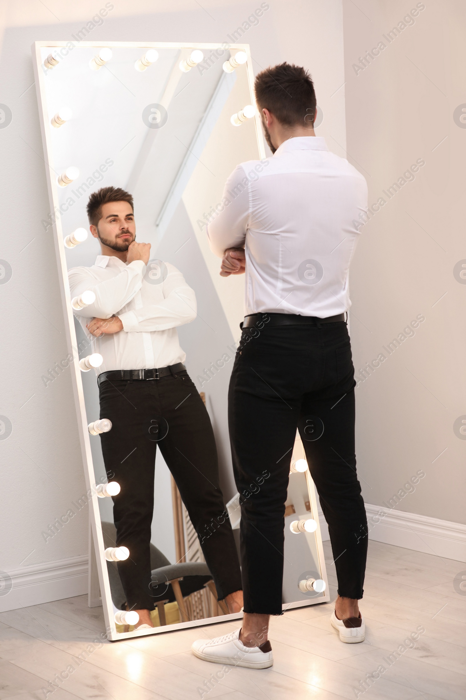 Photo of Young man looking at himself in large mirror at home