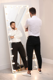 Young man looking at himself in large mirror at home
