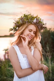 Photo of Young woman wearing wreath made of beautiful flowers outdoors