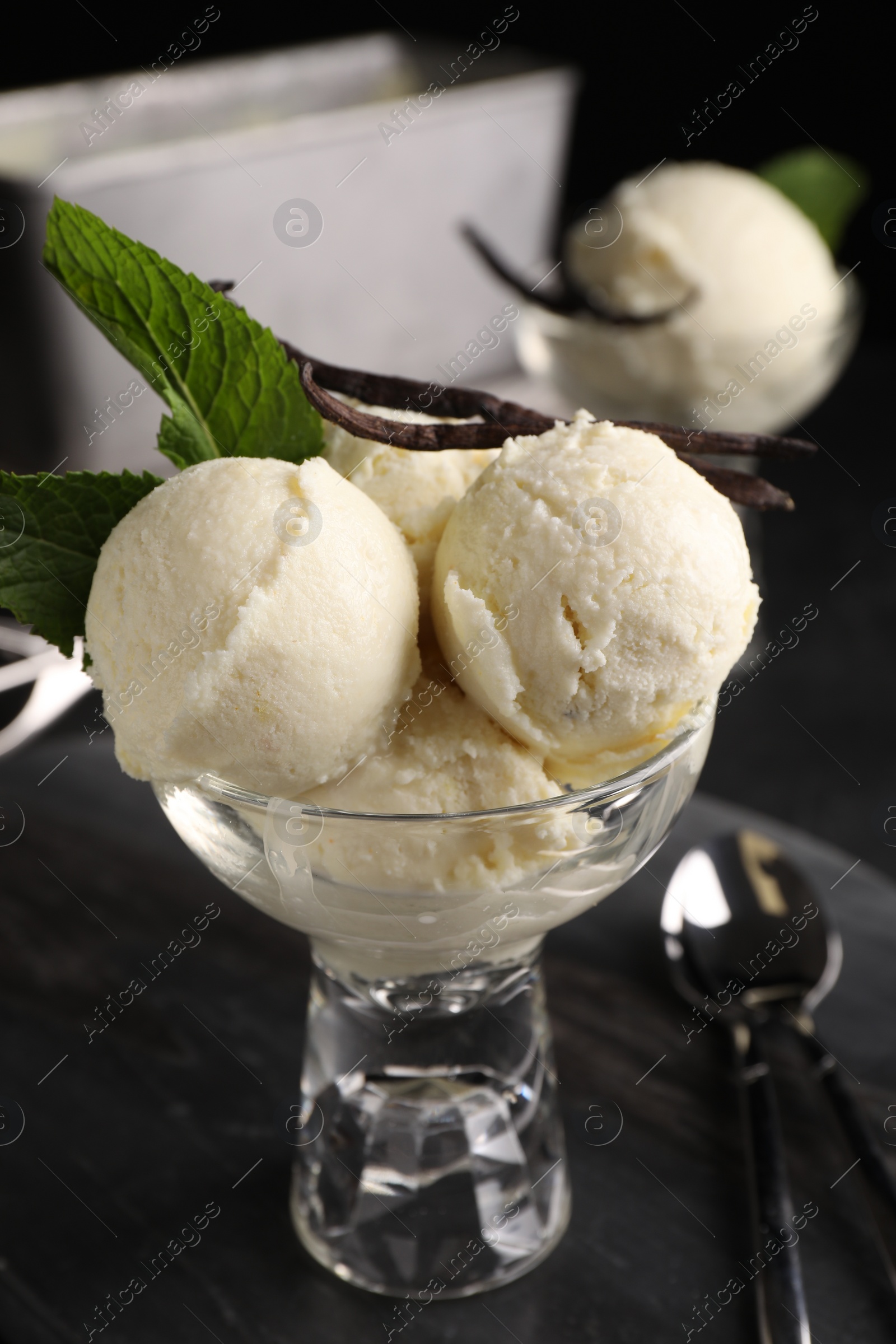 Photo of Tasty ice cream with vanilla pods and mint in glass dessert bowl on dark grey table, closeup