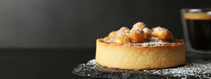 Delicious tartlet with hazelnuts, sweet caramel and powdered sugar on black table, space for text. Banner design