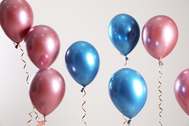 Photo of Bright balloons with ribbons flying on light background