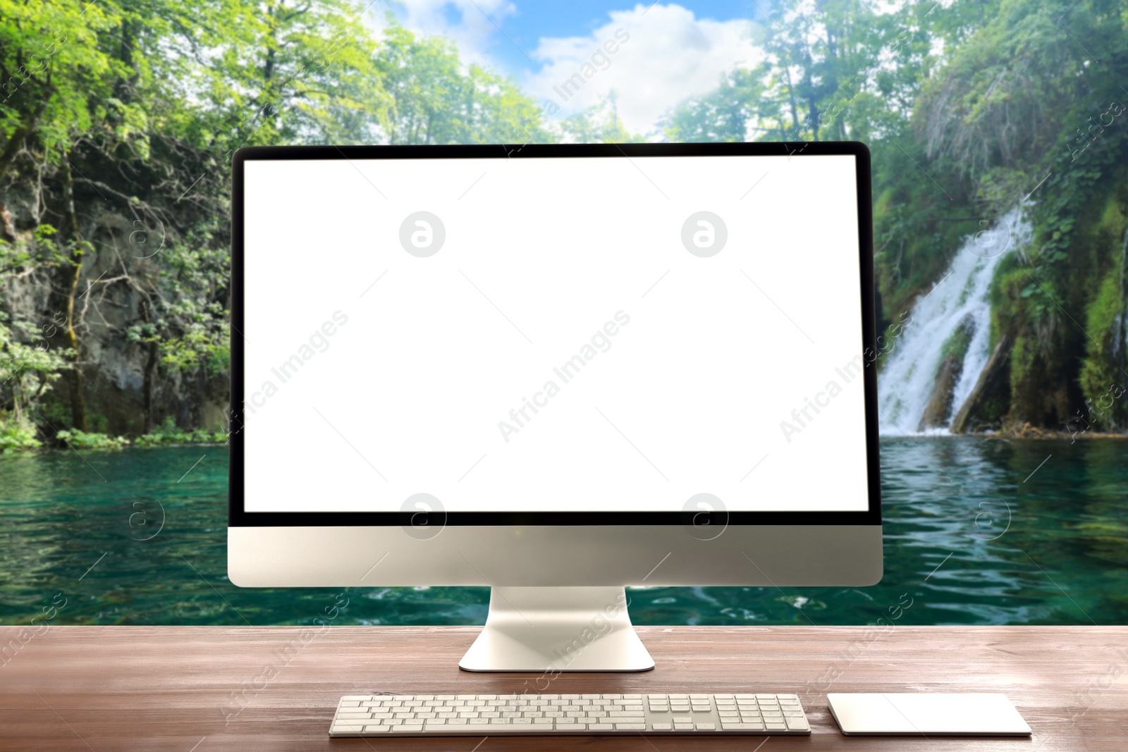 Image of Modern computer with blank screen on white table and view of beautiful waterfall and lake