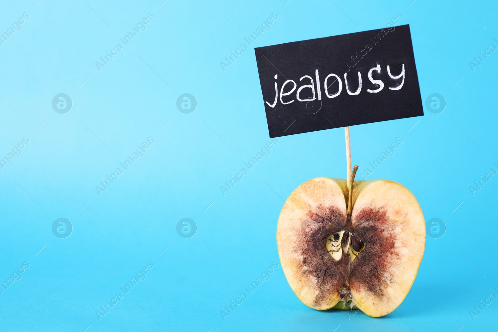 Photo of Rotten apple with JEALOUSY sign on light blue background. Space for text