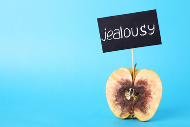 Photo of Rotten apple with JEALOUSY sign on light blue background. Space for text