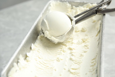 Container and scoop with delicious vanilla ice cream on table, closeup