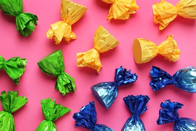 Photo of Candies in colorful wrappers on pink background, flat lay