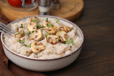 Photo of Delicious barley porridge with mushrooms and microgreens in bowl on wooden table, closeup