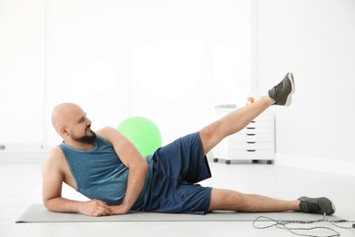 Overweight man doing exercise on mat in gym