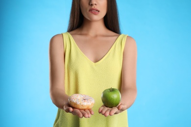 Photo of Concept of choice. Woman holding apple and doughnut on light blue background, closeup