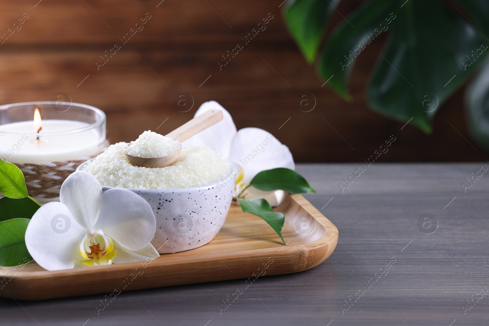 Photo of Natural sea salt in bowl, candle and beautiful orchid flower on wooden table. Space for text