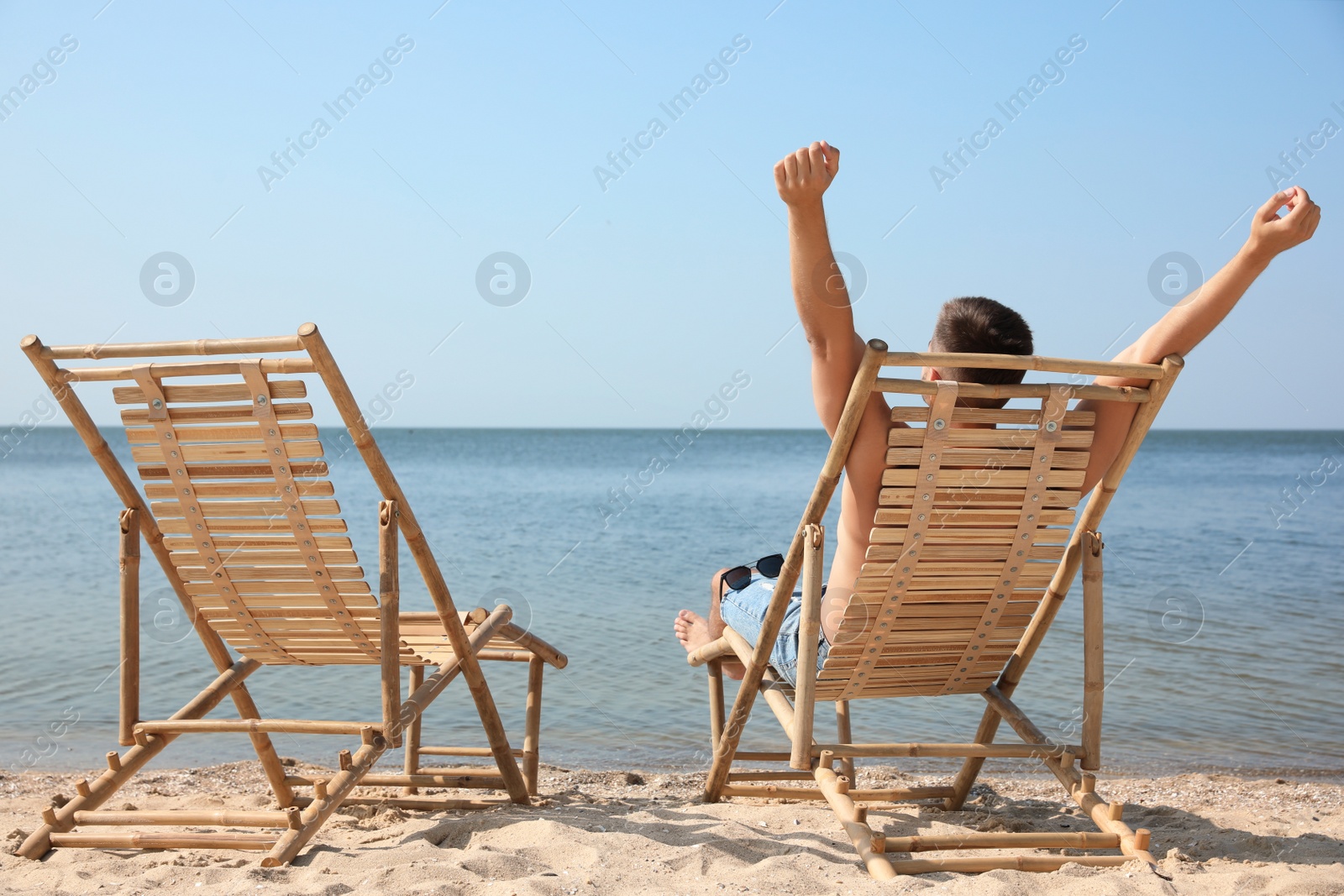 Photo of Young man relaxing in deck chair on sandy beach