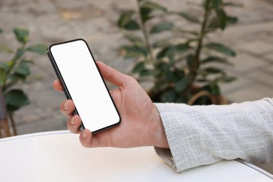 Man using smartphone at white table outdoors, closeup