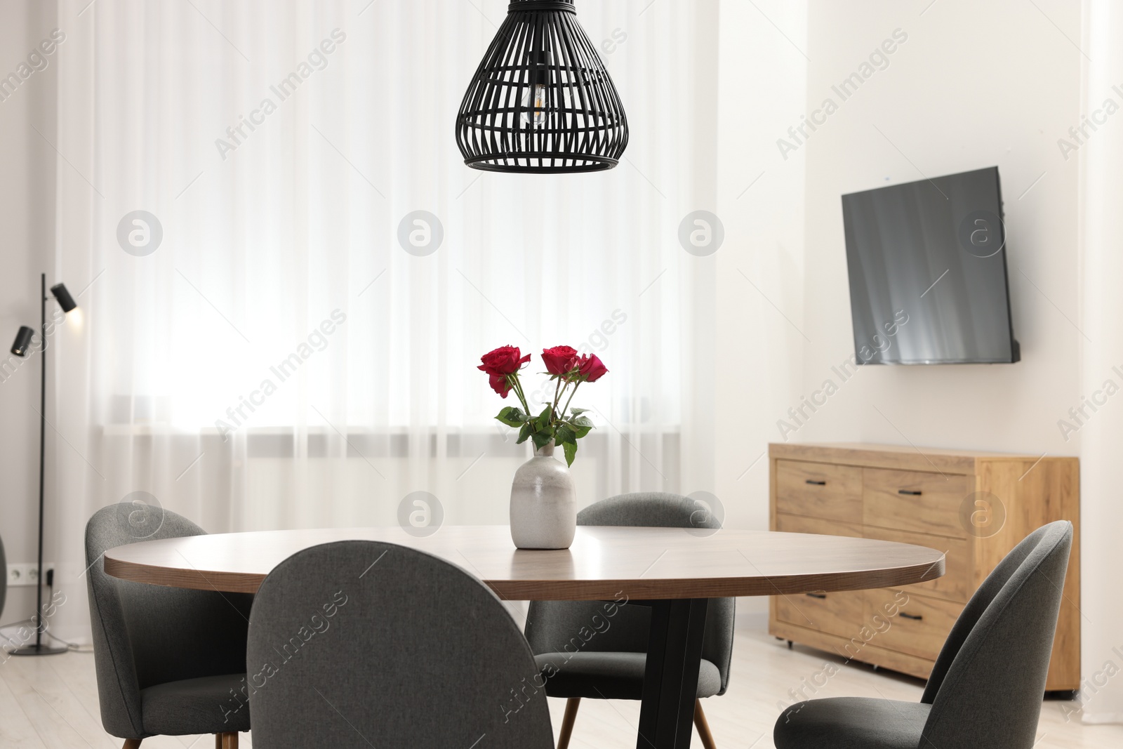 Photo of Chairs and table with vase of red rose flowers in dining room. Stylish interior