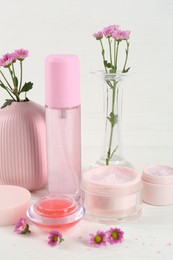 Homemade cosmetic products and beautiful flowers on white wooden table