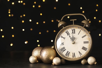 Photo of Vintage alarm clock with decor on black table against blurred Christmas lights, closeup. New Year countdown