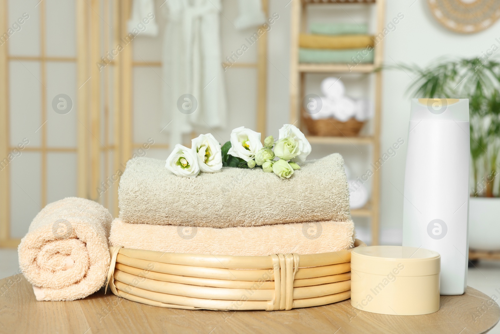 Photo of Soft folded towels, cosmetic products and flowers on wooden table