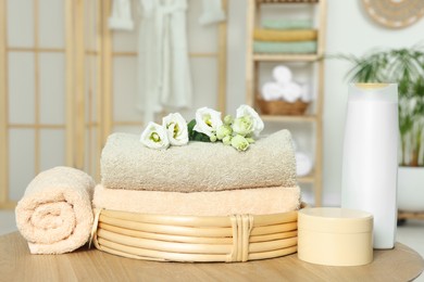 Soft folded towels, cosmetic products and flowers on wooden table