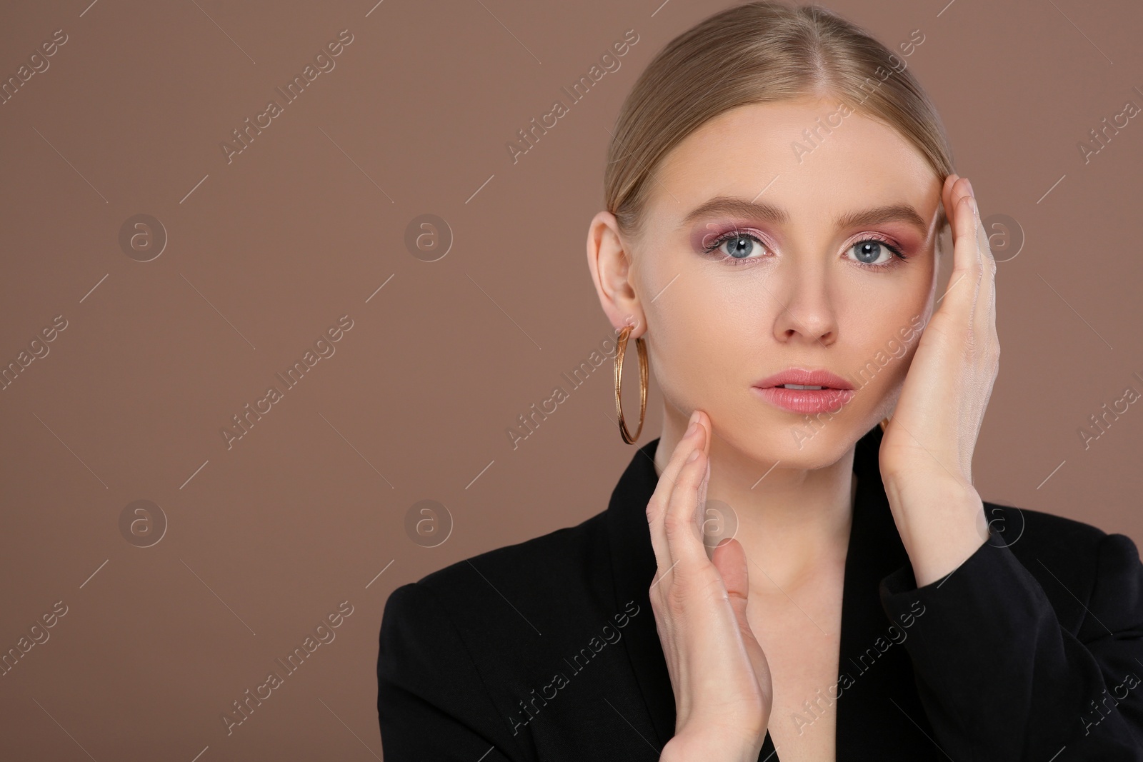 Photo of Beautiful young woman with elegant earrings on light brown background, space for text