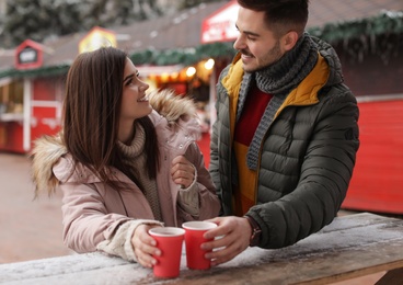 Young couple with cups of mulled wine at winter fair