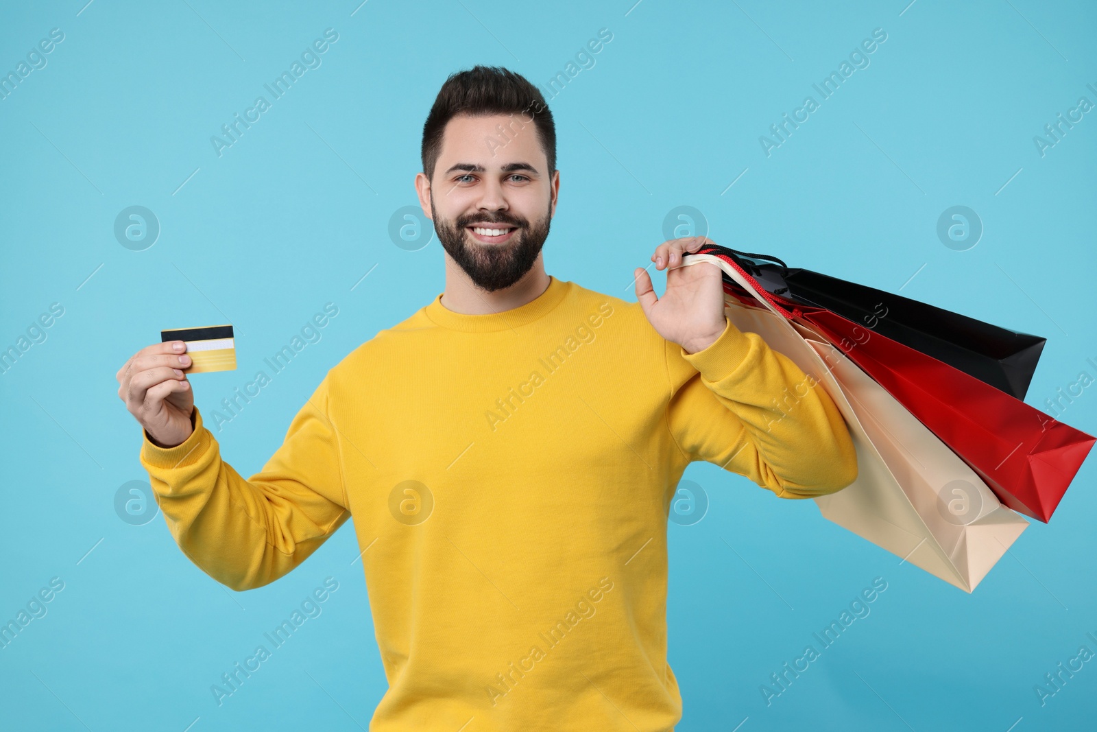 Photo of Smiling man with paper shopping bags showing credit card on light blue background