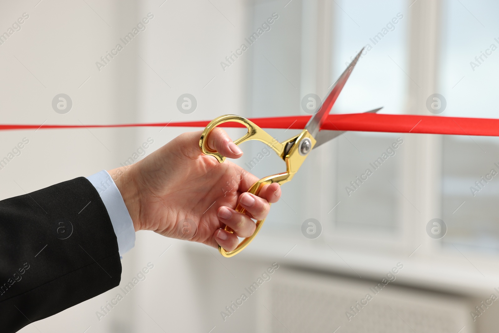 Photo of Woman cutting red ribbon with scissors indoors, closeup