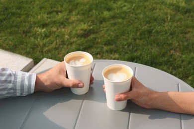 Photo of Coffee to go. Couple with paper cups at grey table outdoors, closeup