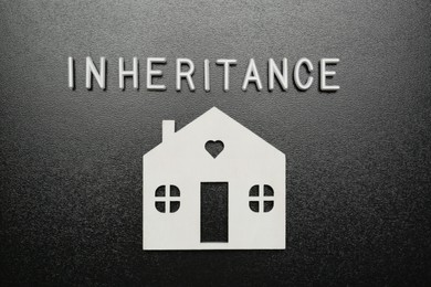 Photo of Word Inheritance made with white letters and house model on black background, flat lay