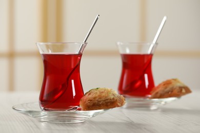 Glasses of traditional Turkish tea and sweet baklava on white wooden table indoors, closeup