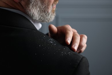 Bearded man brushing dandruff off his jacket on grey background, closeup