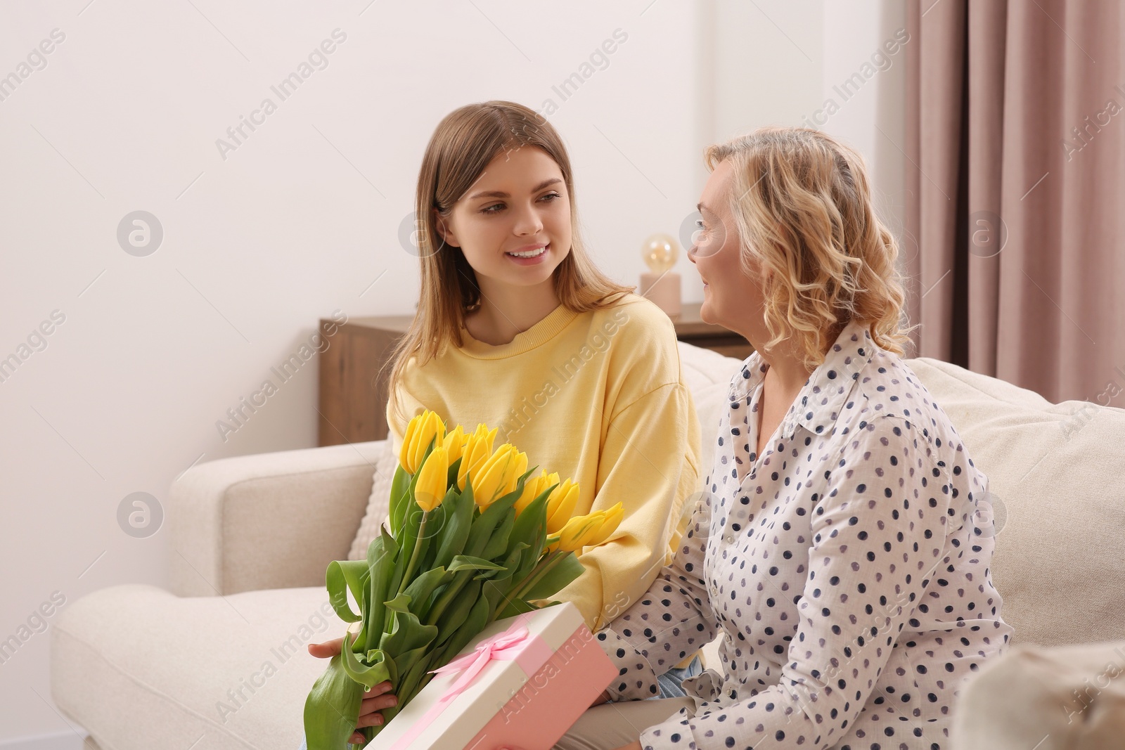 Photo of Young daughter congratulating her mom with flowers and gift at home. Happy Mother's Day