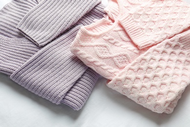 Photo of Stylish knitted sweaters on white fabric, closeup