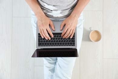 Young man with laptop sitting on floor, top view