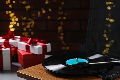 Photo of Turntable with vinyl record and Christmas gift boxes against blurred lights, closeup. Space for text