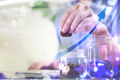 Woman putting money into glass jar at table, closeup