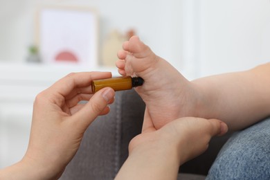 Photo of Mother applying essential oil from roller bottle onto her baby`s heel indoors, closeup