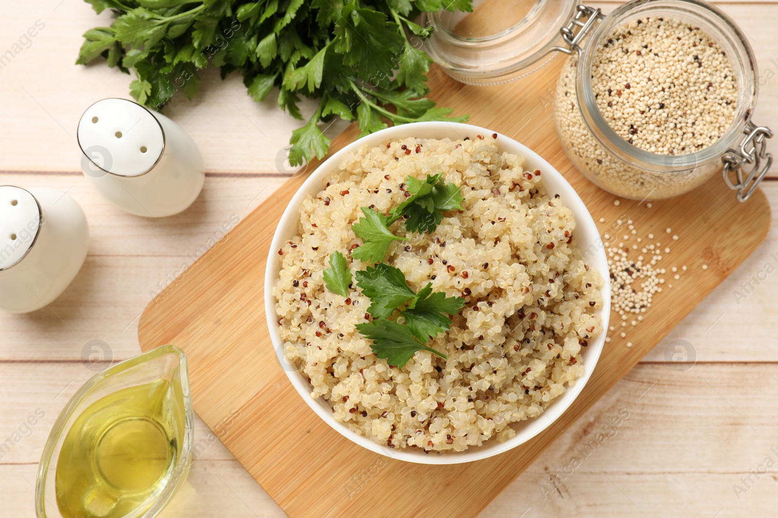 Photo of Tasty quinoa porridge with parsley in bowl and seeds on light wooden table, flat lay