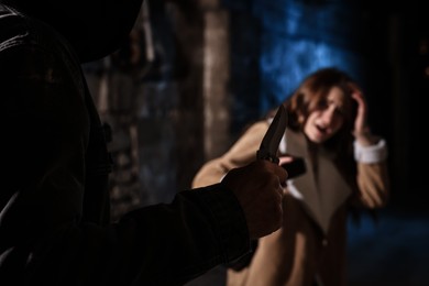 Photo of Criminal threatening young woman with knife in alley at night, focus on hand. Self defense concept