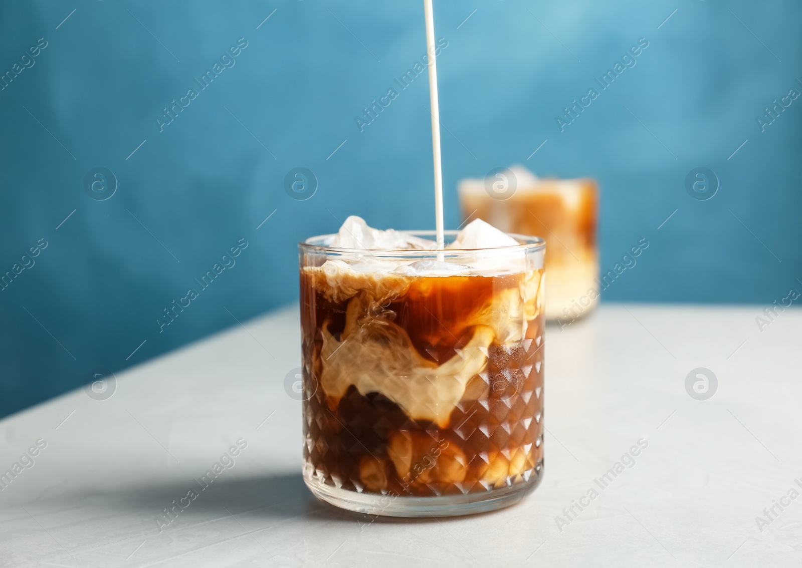 Photo of Pouring milk into glass with cold brew coffee on table