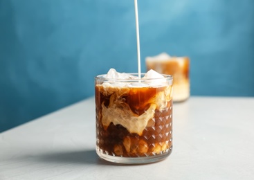 Photo of Pouring milk into glass with cold brew coffee on table