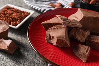 Photo of Pieces of tasty milk chocolate and powder on grey table, closeup